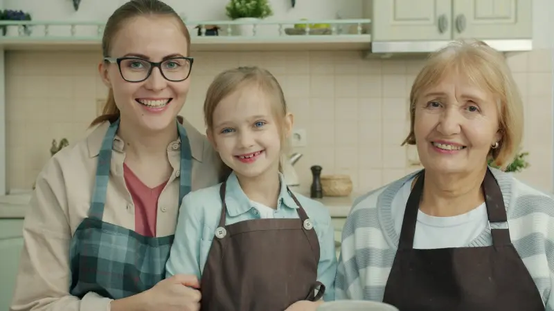 Avó, filha e neta sorrindo juntas na cozinha